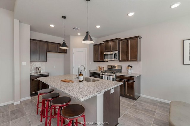 kitchen featuring a center island with sink, appliances with stainless steel finishes, sink, light stone counters, and a breakfast bar area