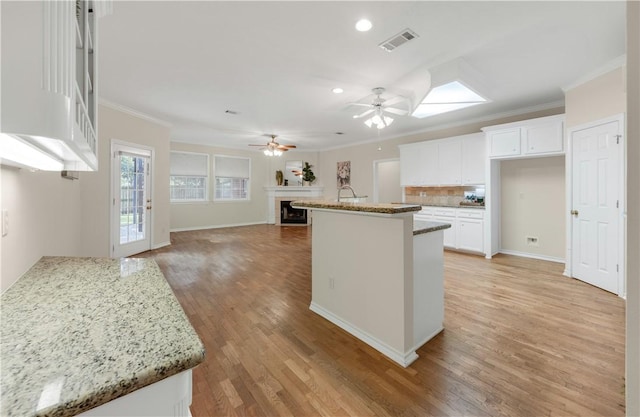 kitchen featuring white cabinetry, a center island, light stone counters, crown molding, and light wood-type flooring