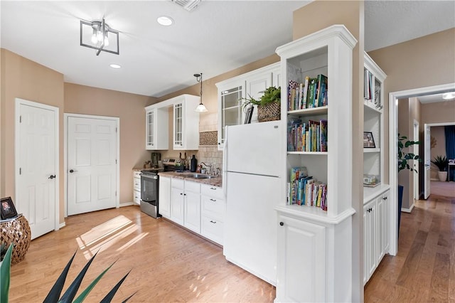 kitchen with light wood-type flooring, white refrigerator, decorative light fixtures, white cabinets, and stainless steel electric range