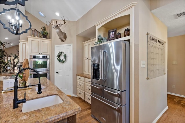 kitchen featuring light stone countertops, cream cabinets, stainless steel appliances, and sink