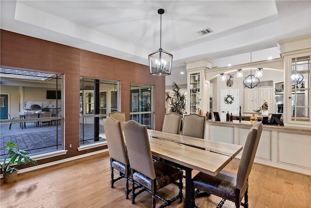 dining space featuring a raised ceiling, an inviting chandelier, and light hardwood / wood-style flooring