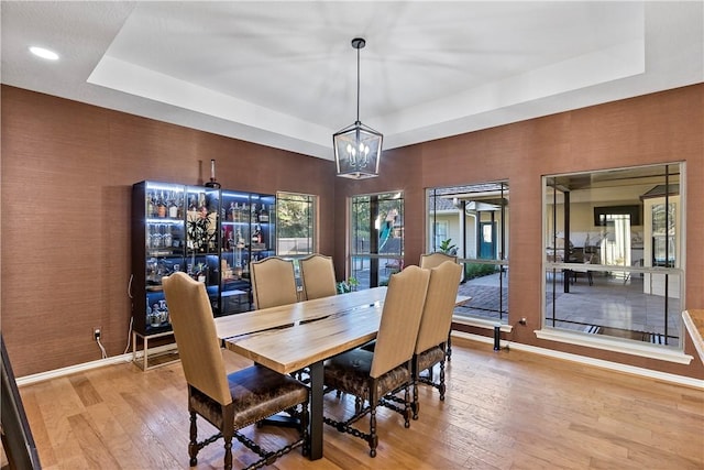 dining space with a notable chandelier, a raised ceiling, and light hardwood / wood-style flooring