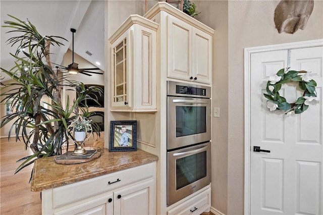 kitchen with light wood-type flooring, double oven, ceiling fan, stone countertops, and vaulted ceiling with beams