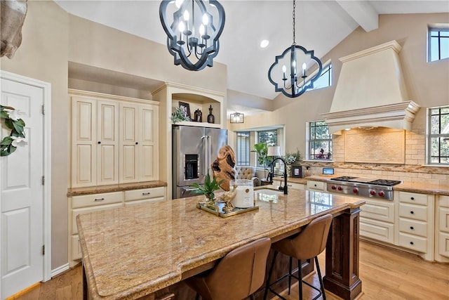 kitchen with lofted ceiling with beams, a kitchen island with sink, stainless steel appliances, and a notable chandelier