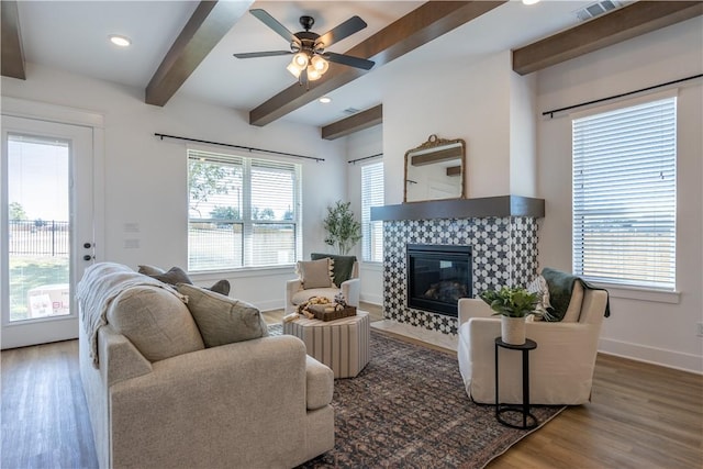 living area featuring beamed ceiling, baseboards, wood finished floors, and a tiled fireplace