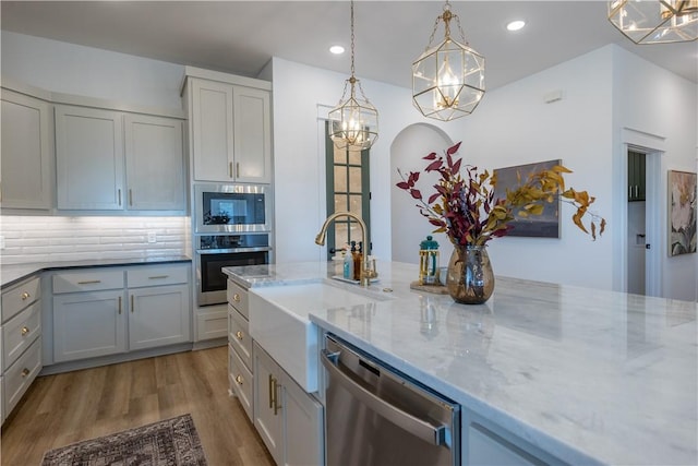 kitchen featuring a sink, tasteful backsplash, wood finished floors, appliances with stainless steel finishes, and light stone countertops