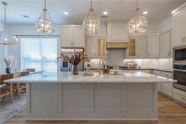 kitchen with light stone countertops, a center island with sink, decorative backsplash, appliances with stainless steel finishes, and a sink