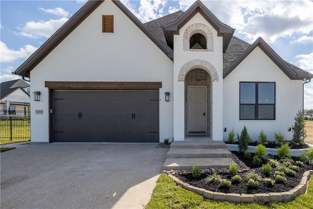 french provincial home with brick siding, fence, concrete driveway, roof with shingles, and a garage