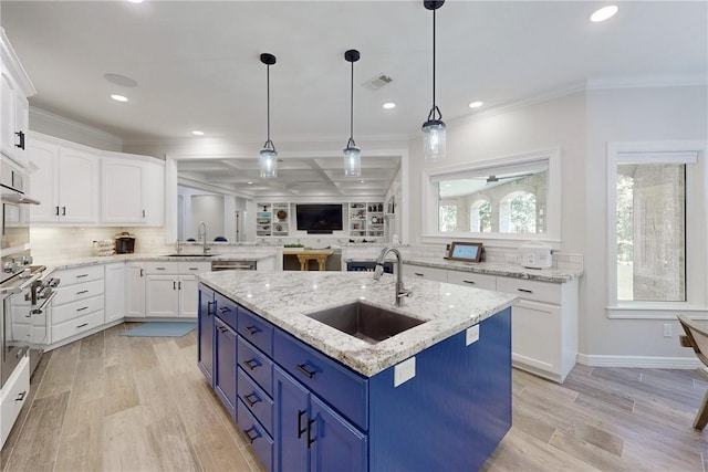 kitchen with blue cabinetry, white cabinetry, sink, and an island with sink