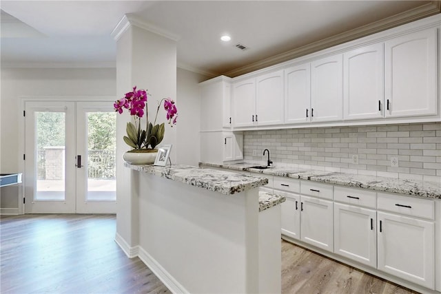 kitchen featuring french doors, backsplash, white cabinetry, and light stone counters