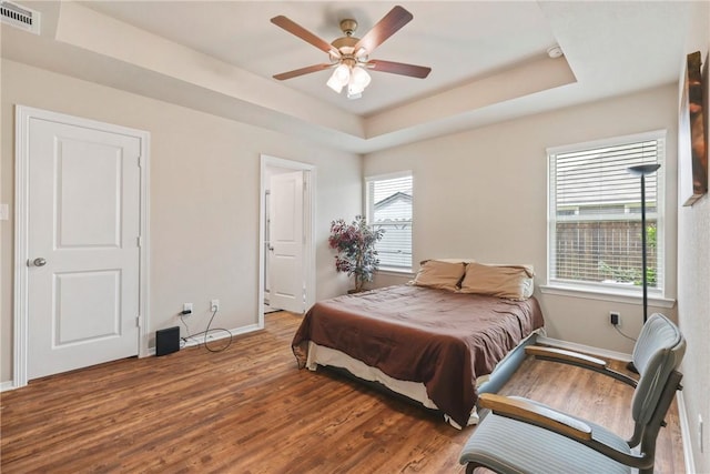 bedroom with visible vents, wood finished floors, baseboards, ceiling fan, and a raised ceiling