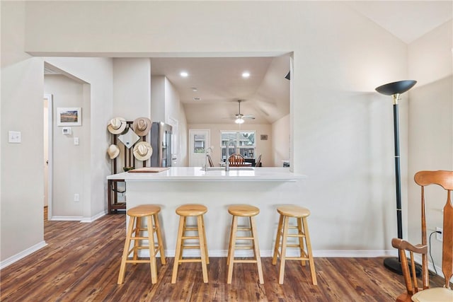 kitchen with a sink, a breakfast bar, vaulted ceiling, and dark wood-type flooring