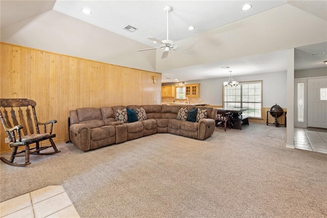living room featuring lofted ceiling, light carpet, wood walls, and ceiling fan with notable chandelier
