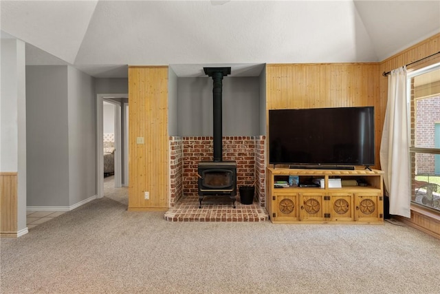 living area with lofted ceiling, wooden walls, a wood stove, baseboards, and carpet flooring