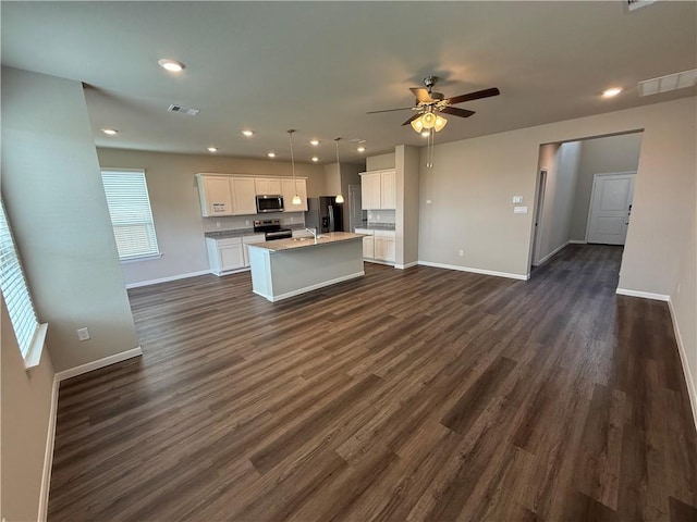 kitchen with appliances with stainless steel finishes, pendant lighting, white cabinets, a kitchen island with sink, and dark wood-type flooring