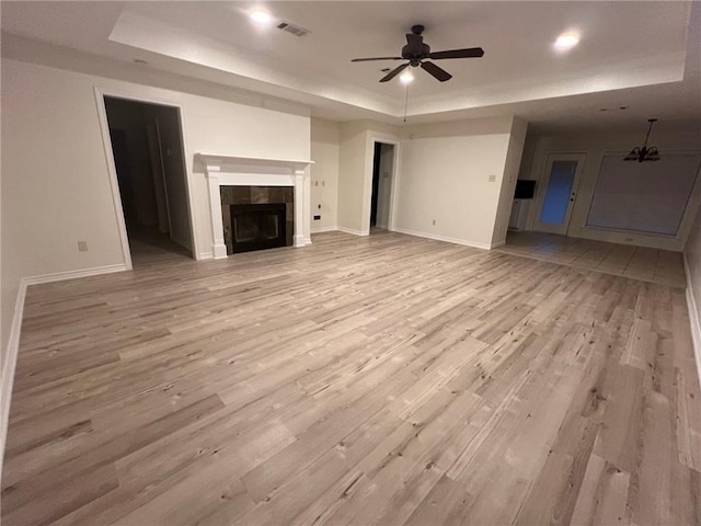 unfurnished living room with light hardwood / wood-style flooring, a tile fireplace, a raised ceiling, and ceiling fan