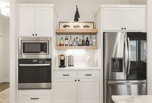 kitchen featuring light stone counters, decorative backsplash, appliances with stainless steel finishes, and white cabinets