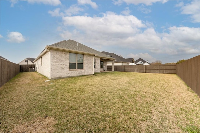 back of house featuring a yard, brick siding, roof with shingles, and a fenced backyard