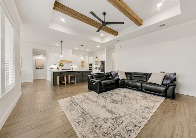 living room with a raised ceiling, light wood-style flooring, baseboards, and beamed ceiling