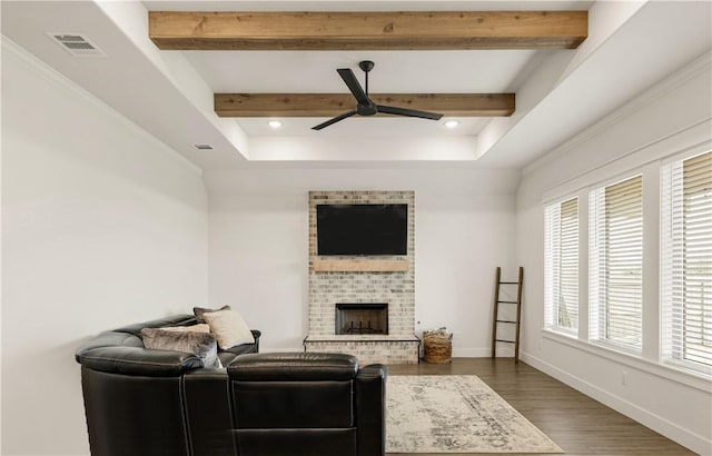 living room featuring visible vents, beamed ceiling, baseboards, a brick fireplace, and ceiling fan