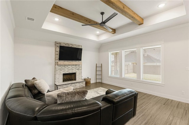 living area with visible vents, a brick fireplace, baseboards, beamed ceiling, and wood finished floors