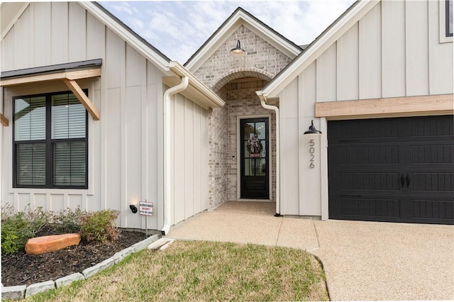 doorway to property with concrete driveway, a garage, brick siding, and board and batten siding