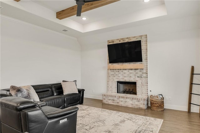 living area featuring beamed ceiling, baseboards, wood finished floors, and a fireplace