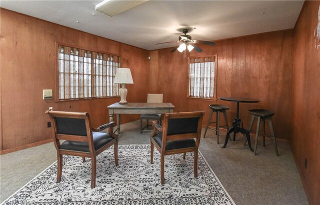 carpeted dining space featuring a wealth of natural light, wooden walls, and ceiling fan