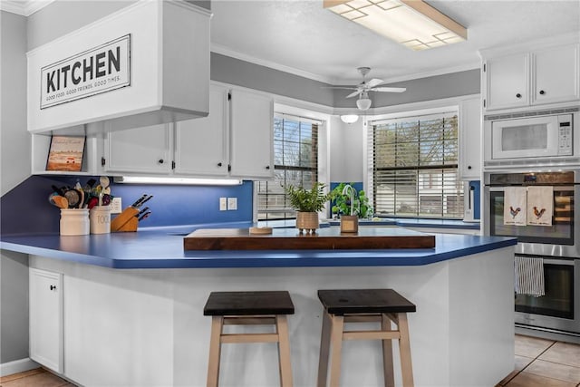 kitchen with white cabinetry, white microwave, double oven, and kitchen peninsula