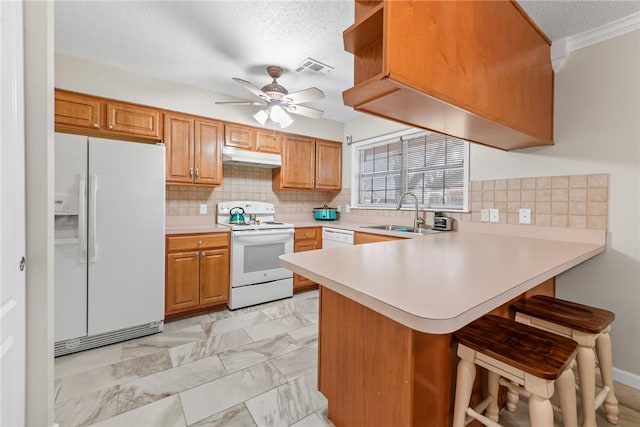 kitchen featuring sink, white appliances, ceiling fan, a kitchen breakfast bar, and kitchen peninsula