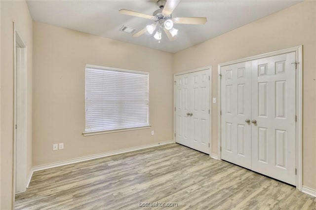 unfurnished bedroom with ceiling fan, light hardwood / wood-style floors, and two closets