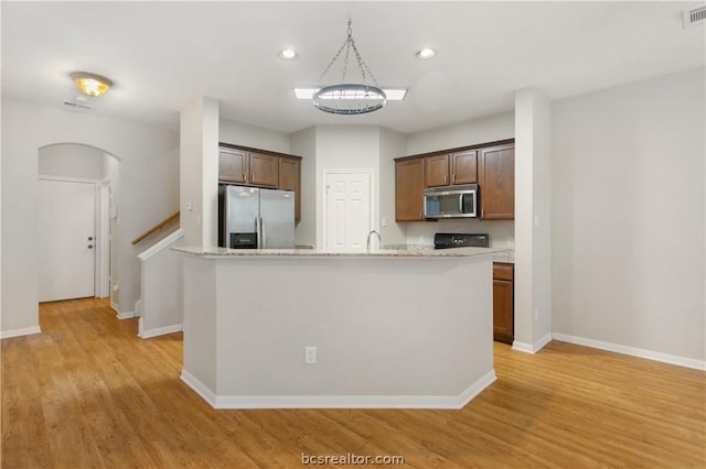 kitchen featuring pendant lighting, a kitchen island with sink, light stone countertops, light wood-type flooring, and stainless steel appliances