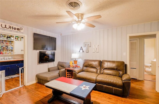 living area featuring ceiling fan, visible vents, a textured ceiling, and light wood-style flooring