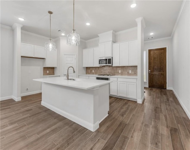 kitchen with a center island with sink, crown molding, sink, decorative light fixtures, and white cabinetry