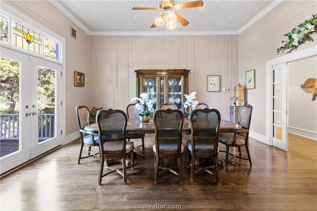 dining space featuring dark wood-type flooring, french doors, crown molding, wooden walls, and ceiling fan