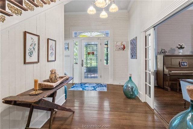 foyer with wood walls, crown molding, dark wood-type flooring, and a notable chandelier