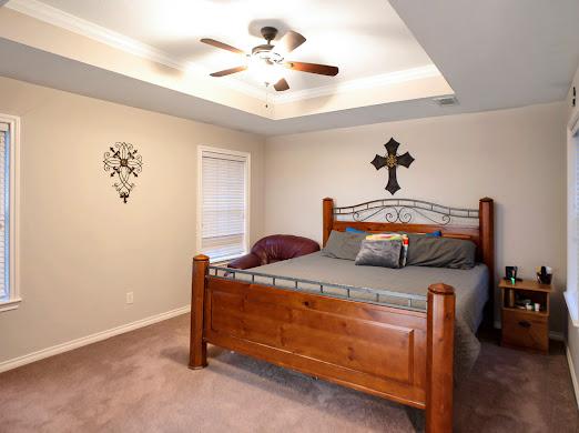 carpeted bedroom with ceiling fan, a raised ceiling, and ornamental molding