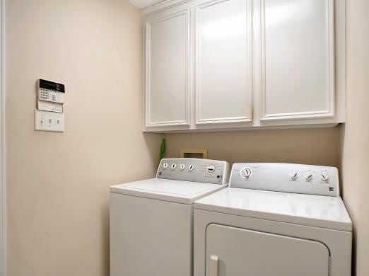 clothes washing area with washer and clothes dryer and cabinets