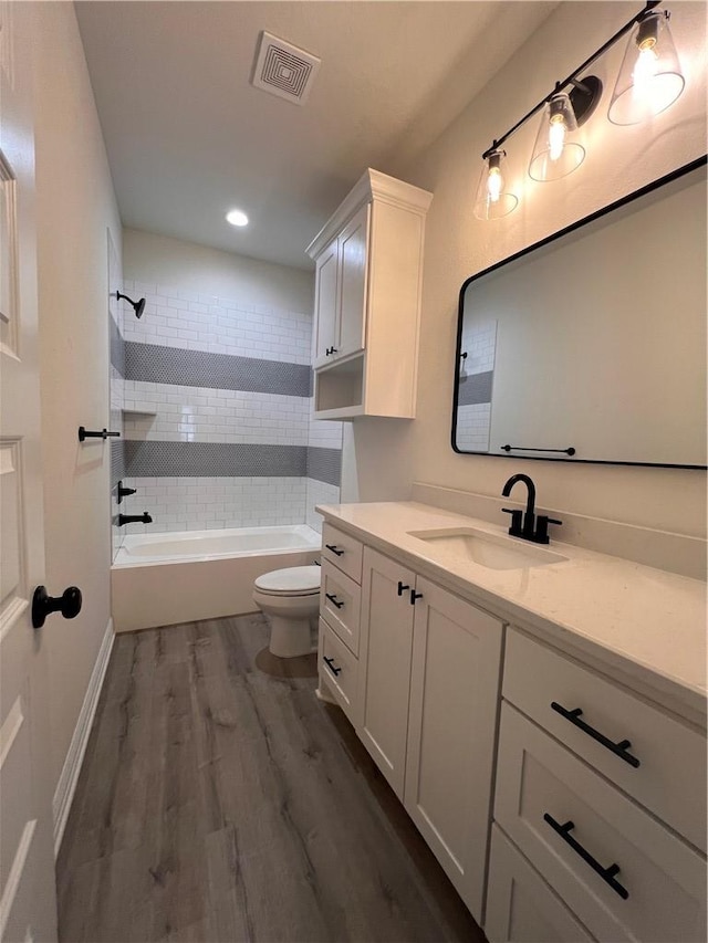 full bathroom featuring vanity, hardwood / wood-style floors, tiled shower / bath combo, and toilet