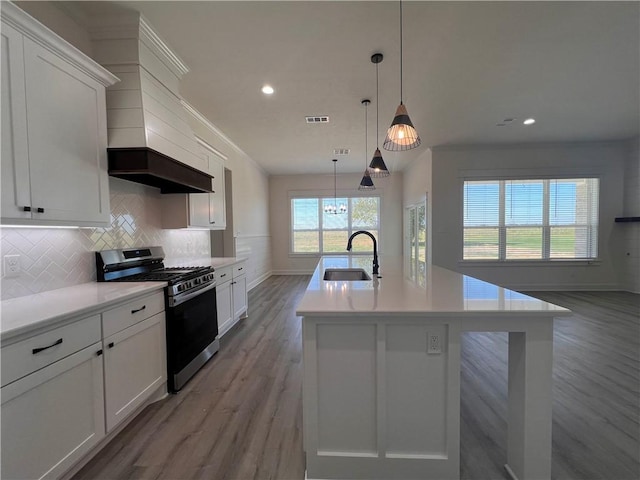 kitchen featuring sink, stainless steel range with gas cooktop, an island with sink, pendant lighting, and light hardwood / wood-style floors