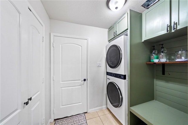 laundry area with stacked washer / drying machine, a textured ceiling, light tile patterned floors, and cabinets