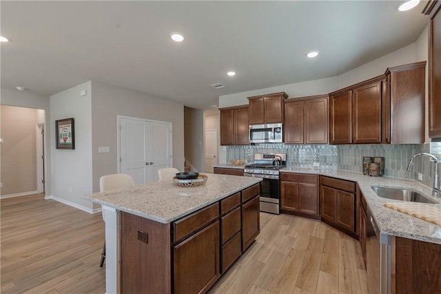 kitchen featuring stainless steel appliances, light stone countertops, a sink, and a kitchen island