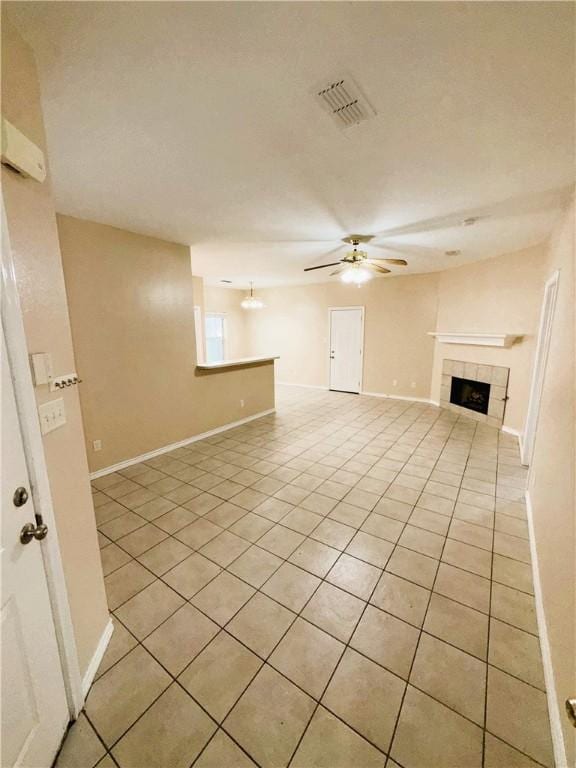 unfurnished living room featuring light tile patterned floors, visible vents, a tiled fireplace, a ceiling fan, and baseboards