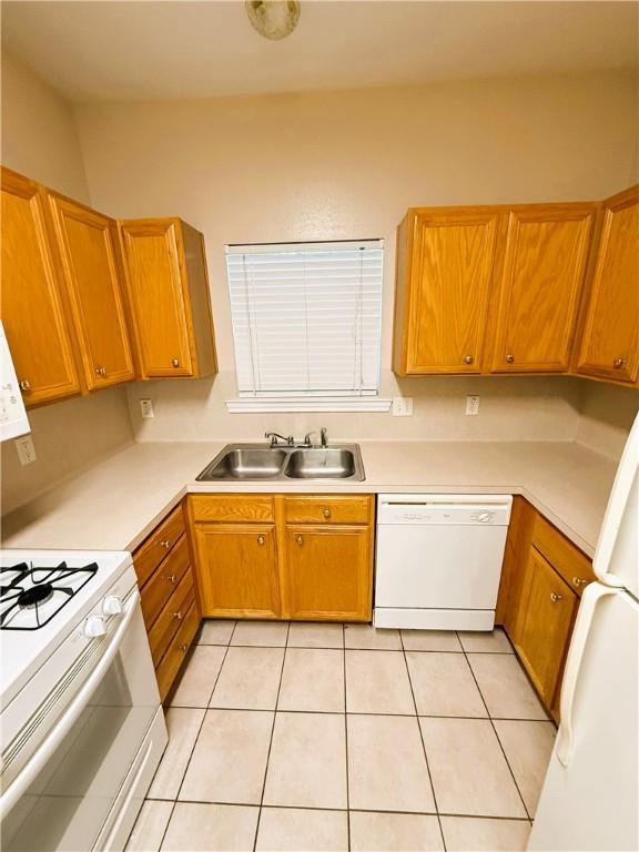 kitchen featuring light countertops, white appliances, brown cabinetry, and a sink