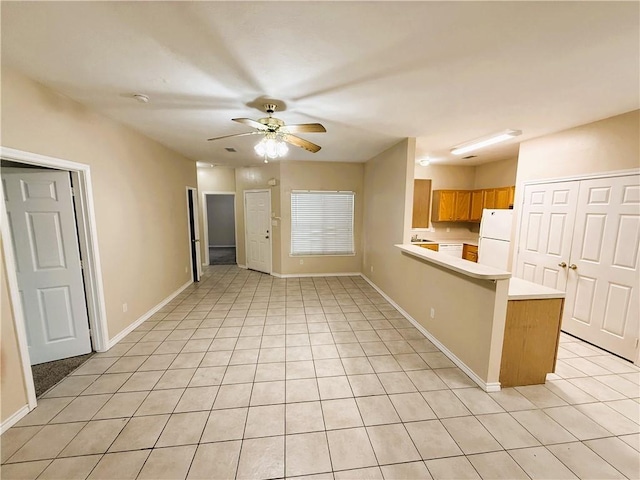 kitchen with brown cabinets, freestanding refrigerator, a peninsula, light countertops, and light tile patterned flooring