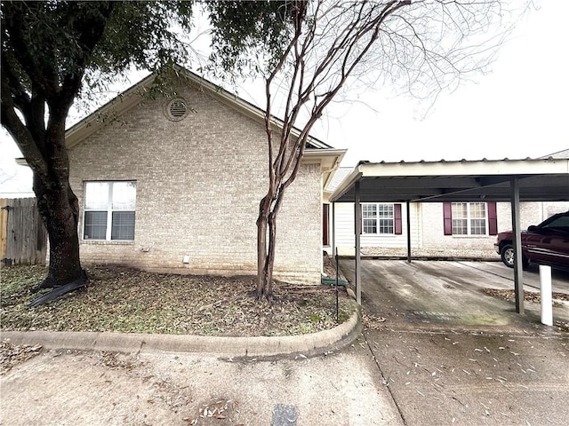 view of side of home featuring a carport, brick siding, and fence