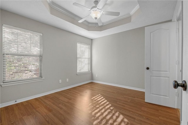 empty room with wood finished floors, a raised ceiling, baseboards, and ornamental molding