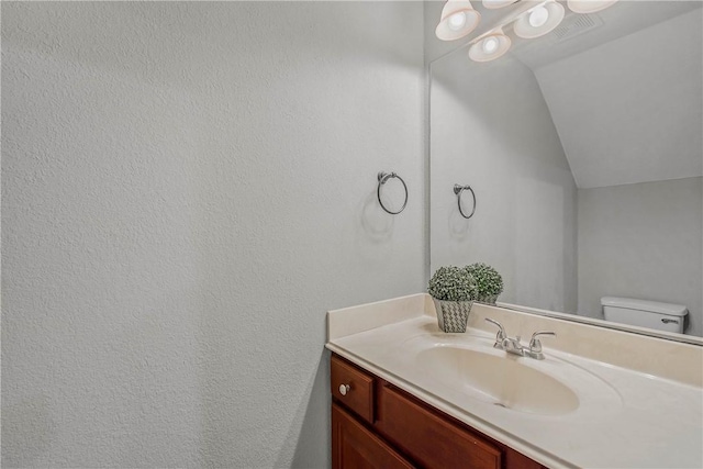 bathroom featuring visible vents, lofted ceiling, toilet, and vanity