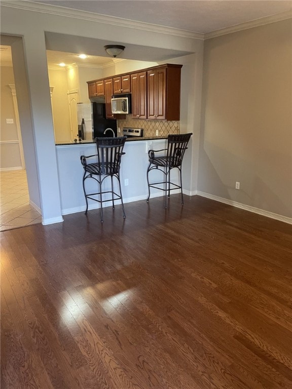 kitchen featuring ornamental molding, backsplash, dark wood finished floors, appliances with stainless steel finishes, and a breakfast bar area