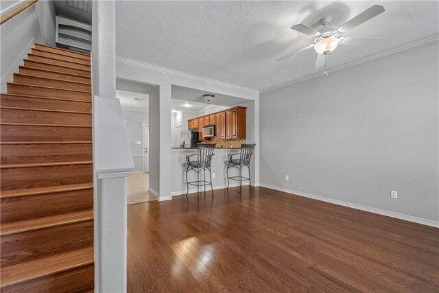 unfurnished living room with a ceiling fan, crown molding, stairway, and dark wood-style floors